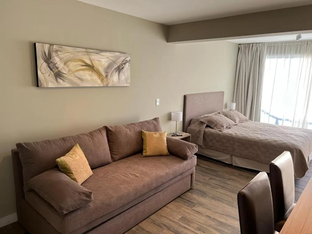 Ambiente único de Güemes 540: sofá cama, cama matrimonial y el ventanal del balcón — el departamento tal cual es